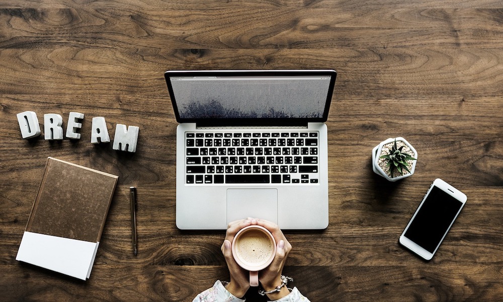 Schreibtisch mit Laptop, Kaffeetasse und Buchstaben DREAM
